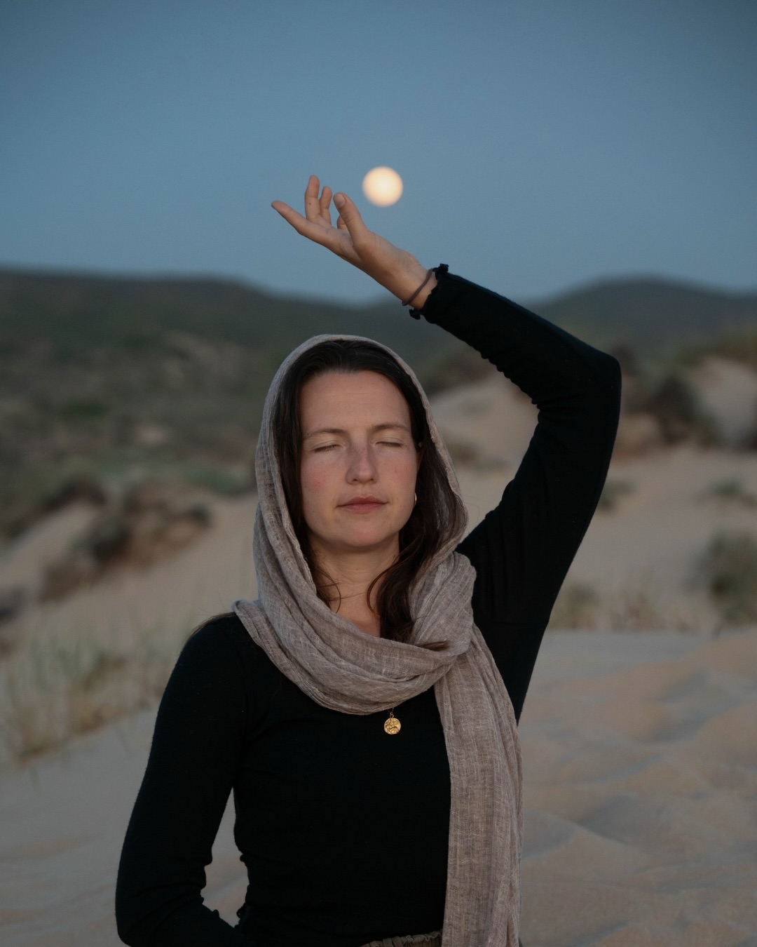 Sara Lonsdorfer, co-founder of Mani Yoga, reaching toward the moon at dusk